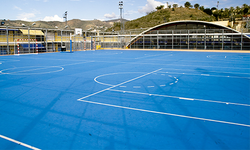 Pista polideportiva azul del Colegio Novaschool Añoreta con el pabellón al fondo